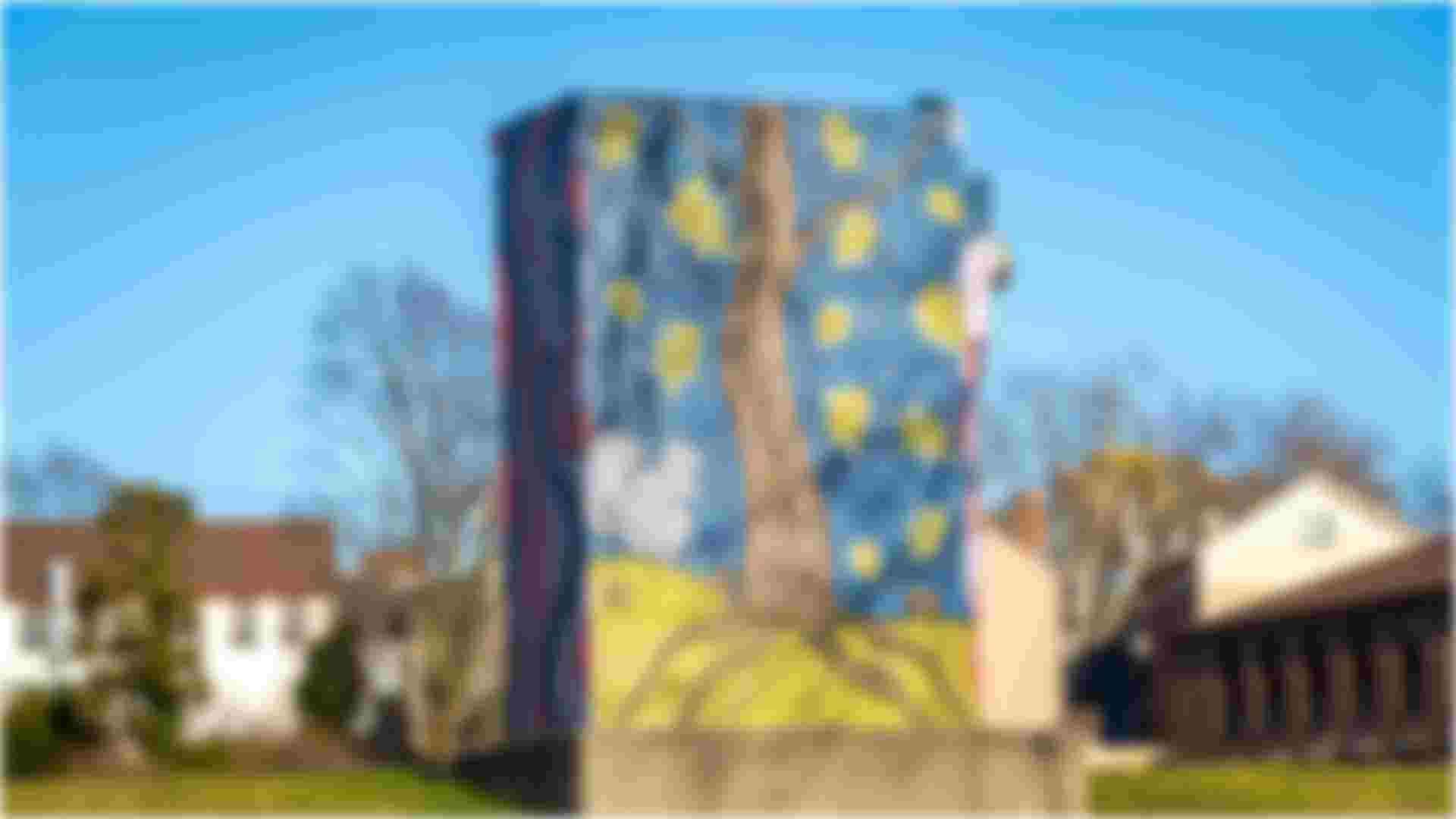 A blue painted utility box with a squirrel and acorns at the base of a tree with leaves falling around the tree. 