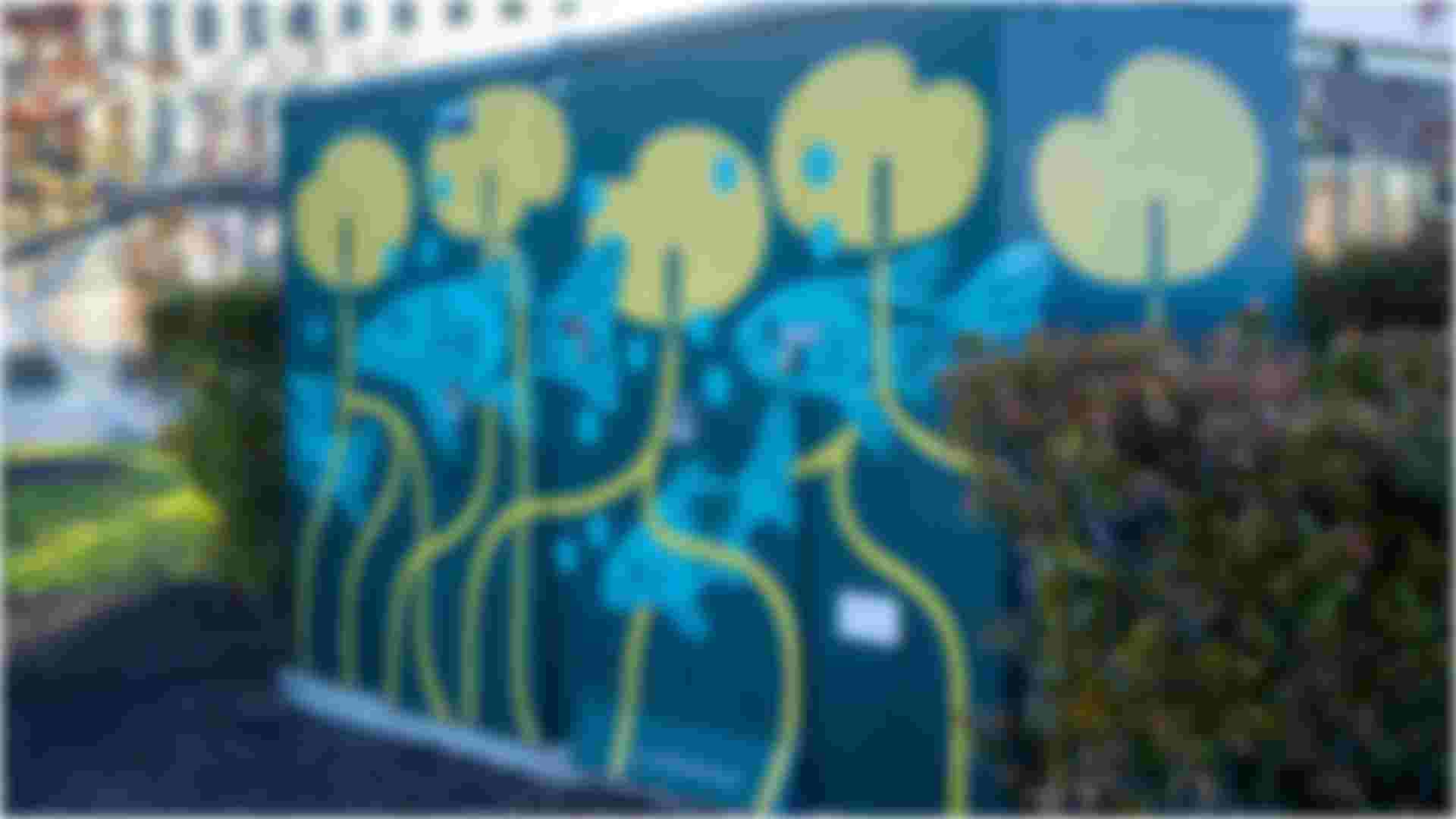 Painted utility box mural showing blue fish swimming among yellow lily pads, on a dark green background.